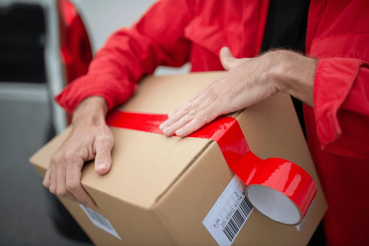 Worker ensuring package security by applying red adhesive tape.