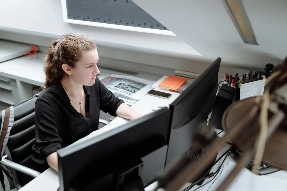 Professional woman reviewing information on dual monitors in a quiet office space.