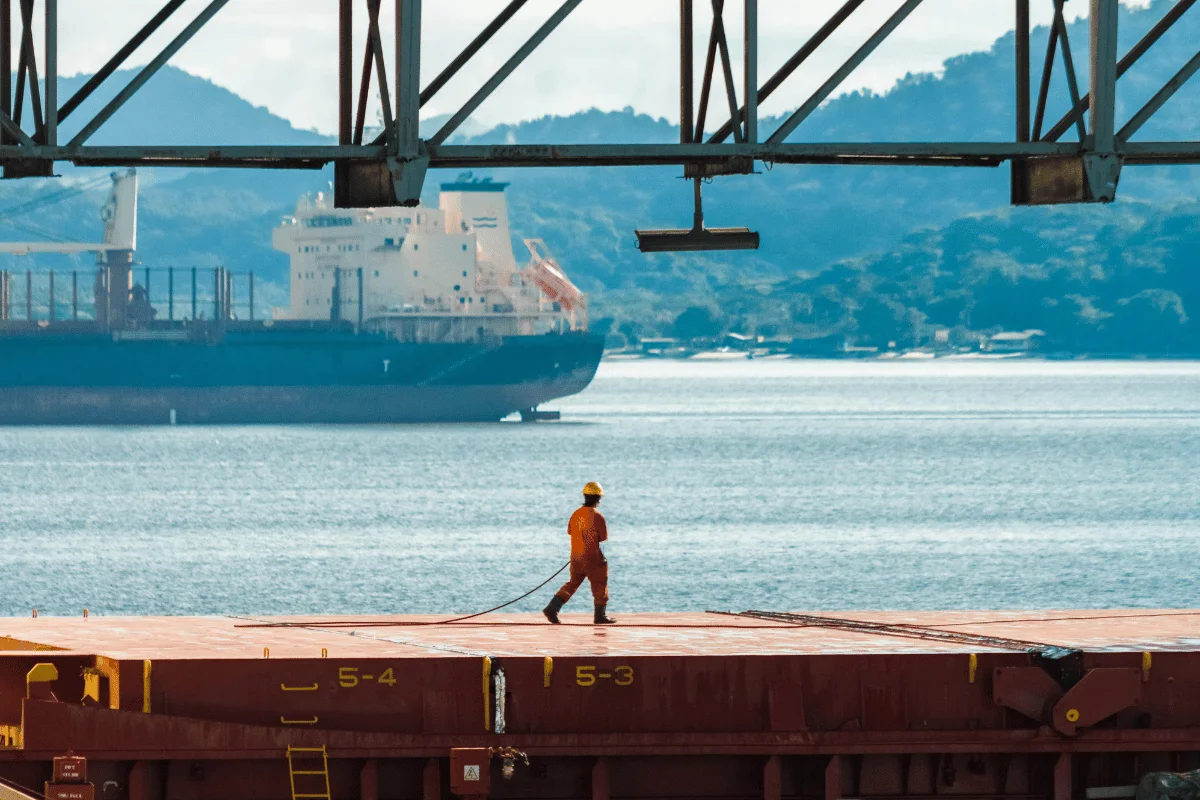 Maritime worker handling cables on a docked ship with a ship in the background.
