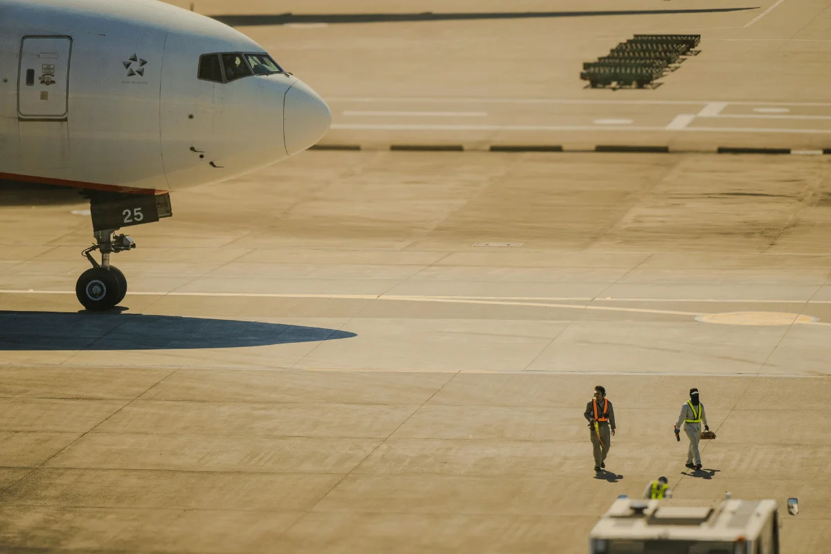 Airport staff inspecting the runway near a stationary aircraft in daylight.