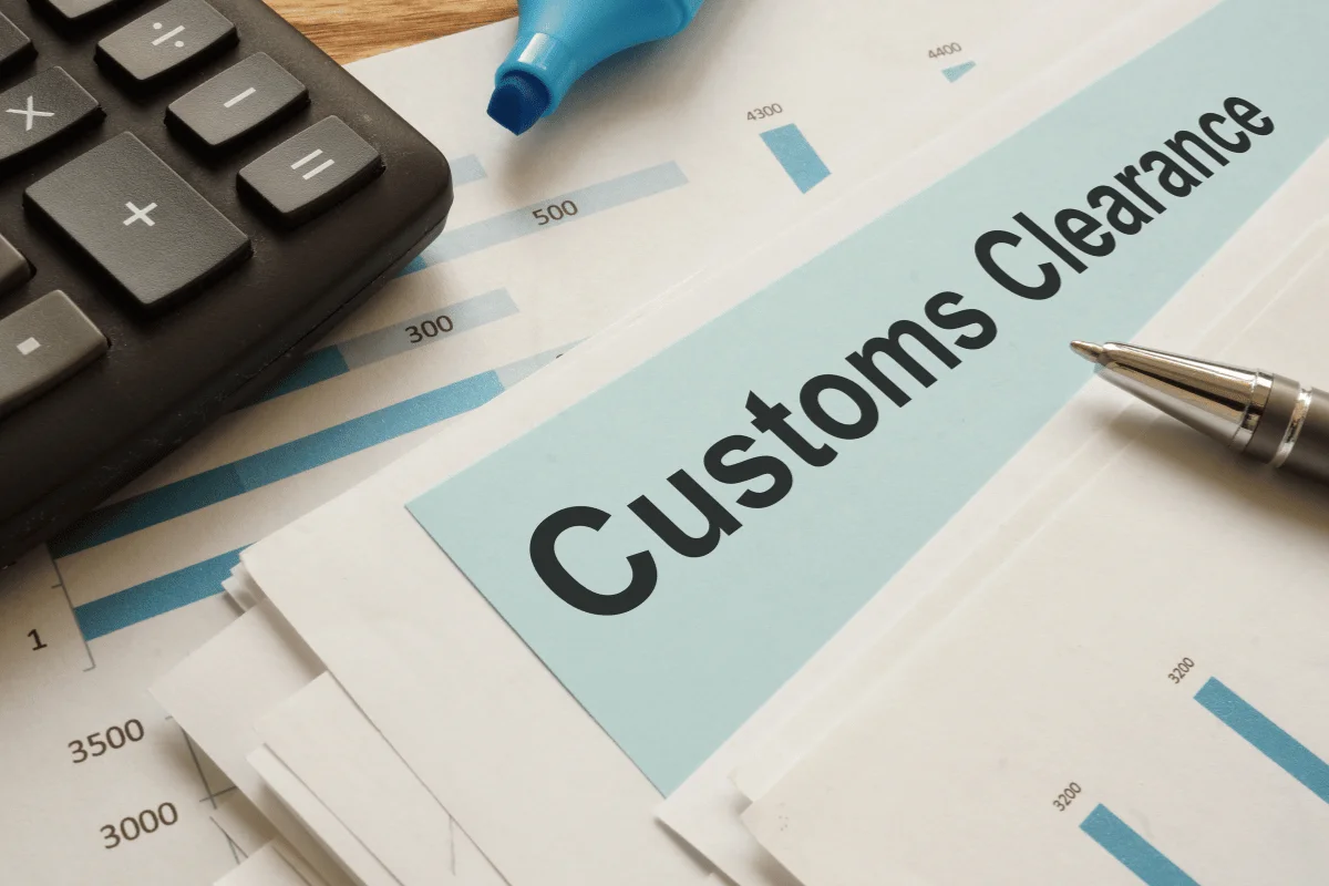 Customs clearance form on a desk with a calculator, pen, and financial charts.