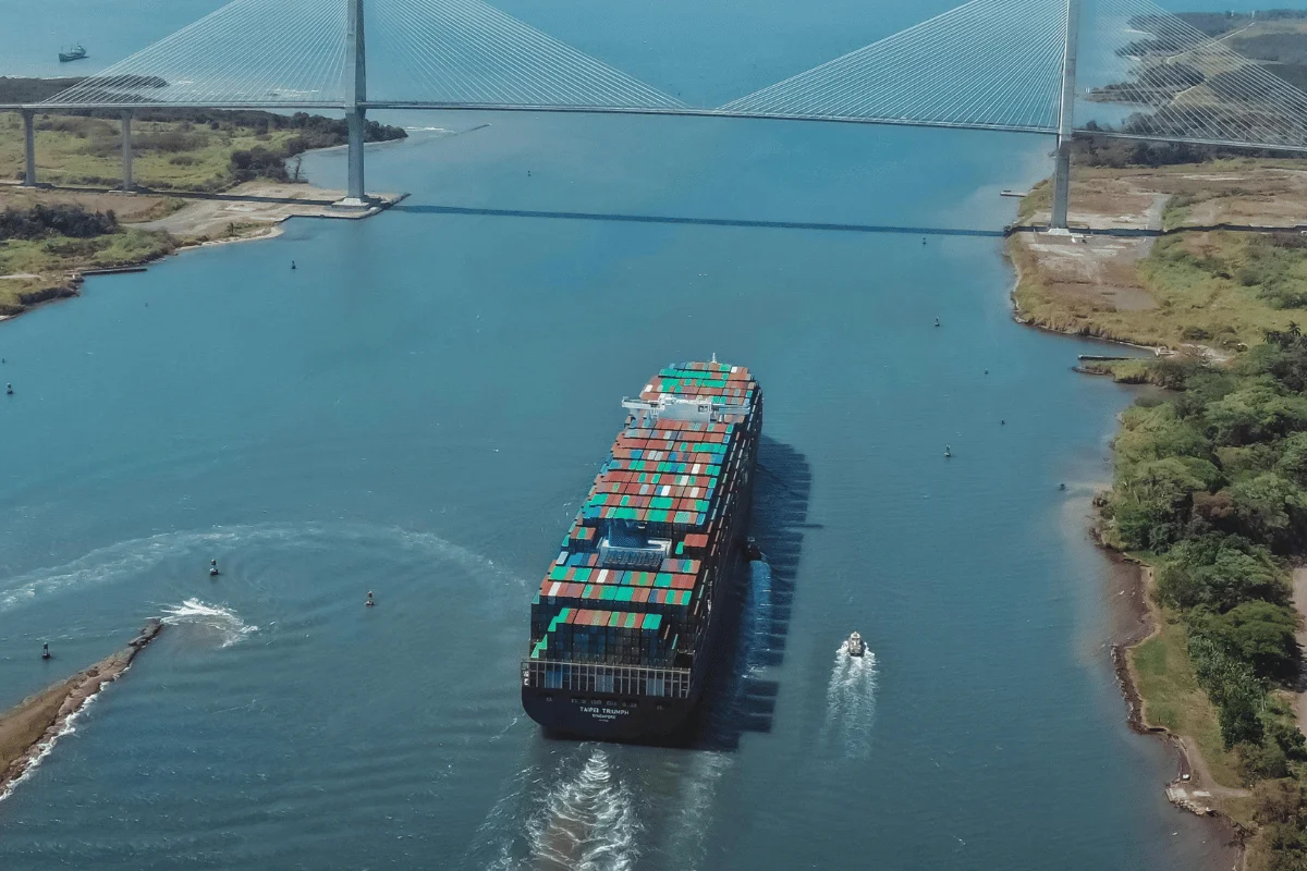 GRI in Shipping: Factors, Impact, and Tactics 11 Large cargo vessel navigating through a canal beneath a modern bridge.