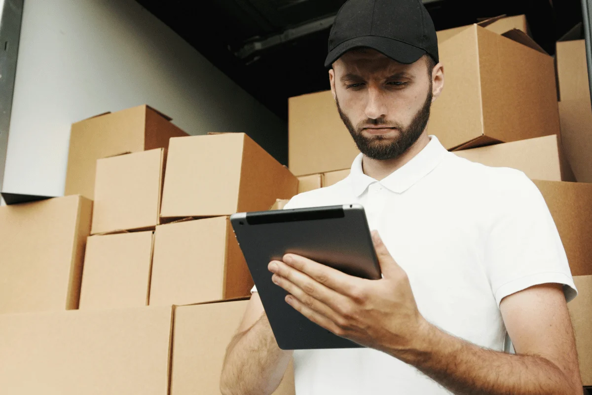 Delivery worker using a tablet in front of a stack of cardboard boxes.