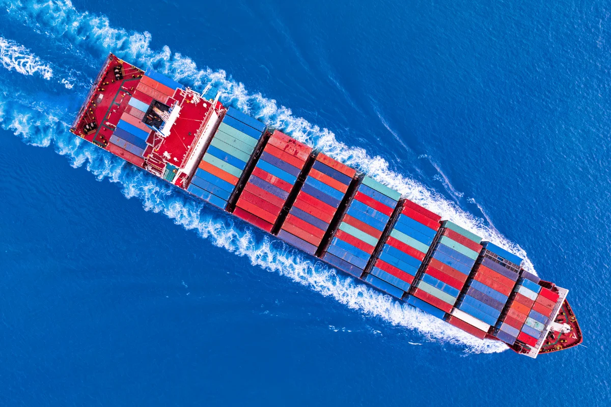 Container ship in motion, displaying stacked cargo containers from an overhead perspective.