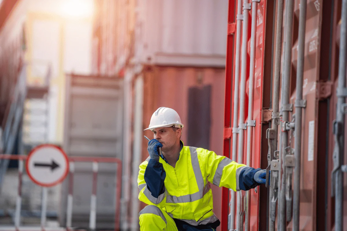 Industrial worker in protective gear checking containers at a port.