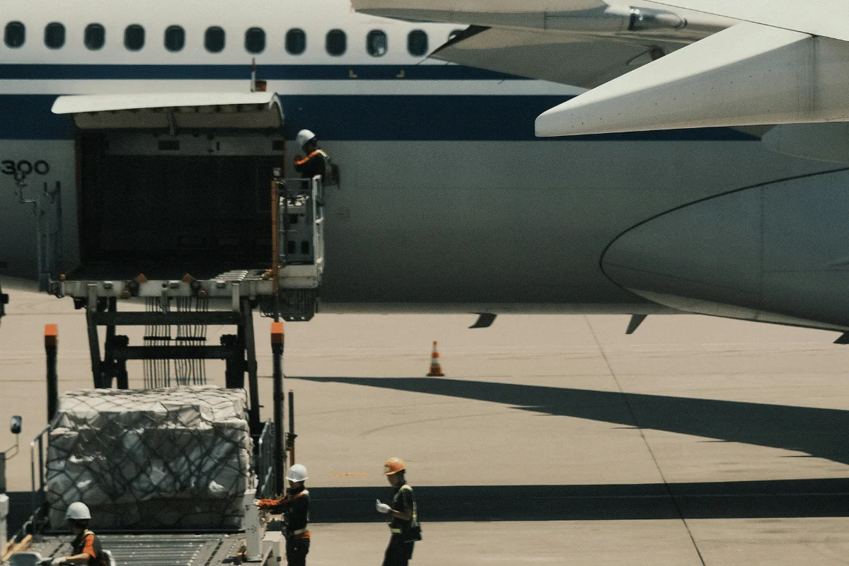 Air Freight Forwarders: Types, Challenges, Solutions & More 7 Ground crew loading cargo onto an airplane at the airport, with workers wearing helmets and safety vests near the aircraft's cargo door.