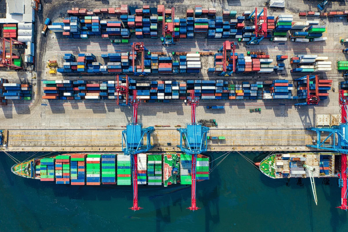 Shipping from Thailand to the USA: Challenges, Solutions & More 9 Aerial view of a busy port with stacked cargo containers and docked ships.