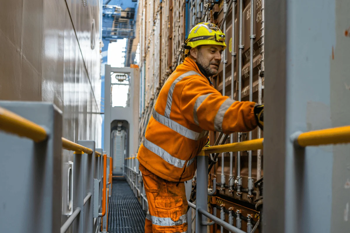 Worker in safety gear inspecting container locks on a ship.