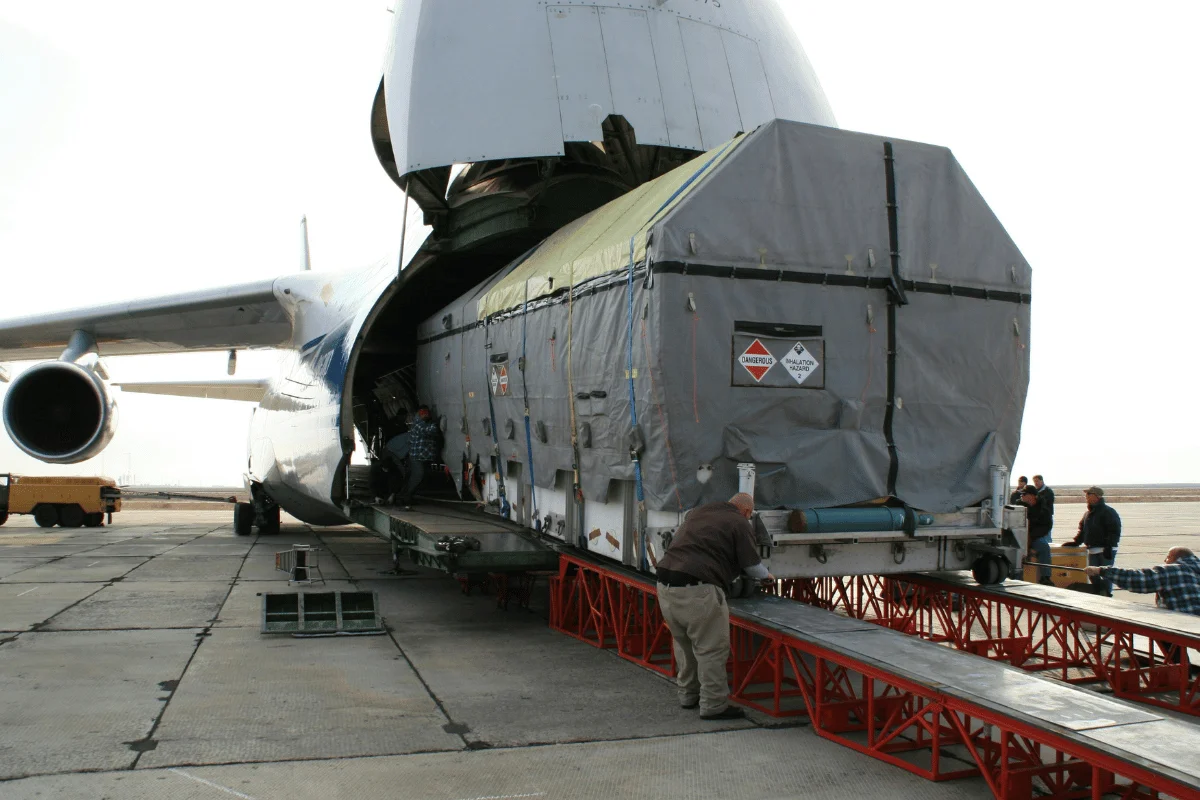 A massive cargo container being loaded into a transport aircraft by a team of workers.