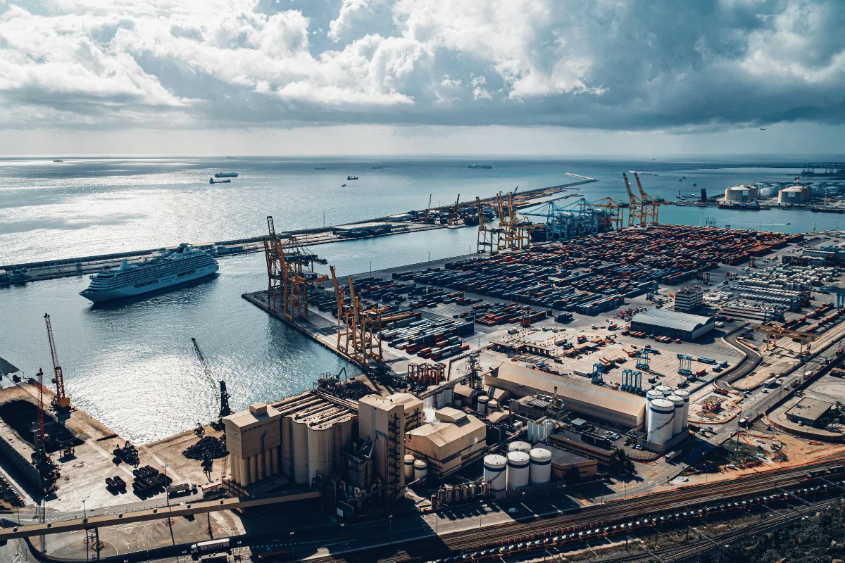 Shipping port filled with cargo containers and cranes, with a cruise ship near the dock.