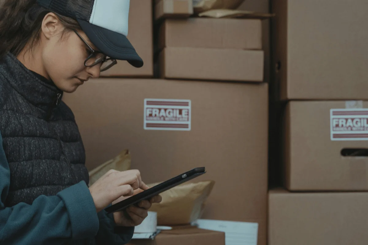 Warehouse employee tracking inventory on a tablet near stacked boxes.