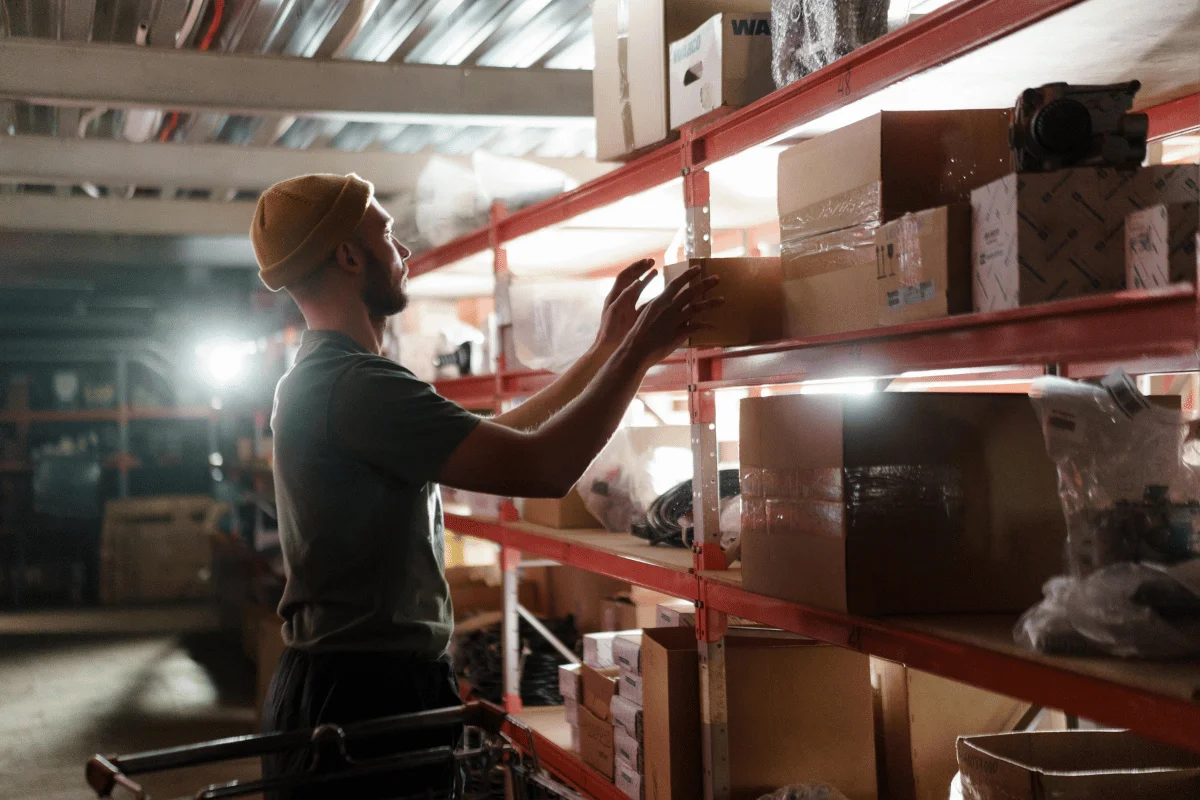 Worker organizing boxes on warehouse shelves under bright lighting.