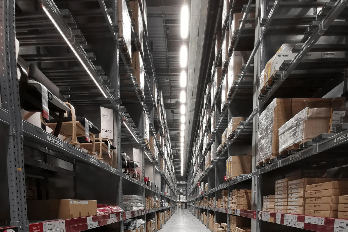 Warehouse aisle with tall storage racks filled with boxes and furniture.