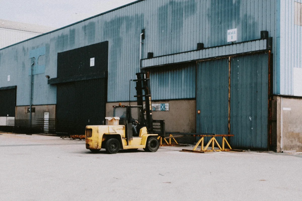 Yellow forklift in front of a large industrial warehouse.