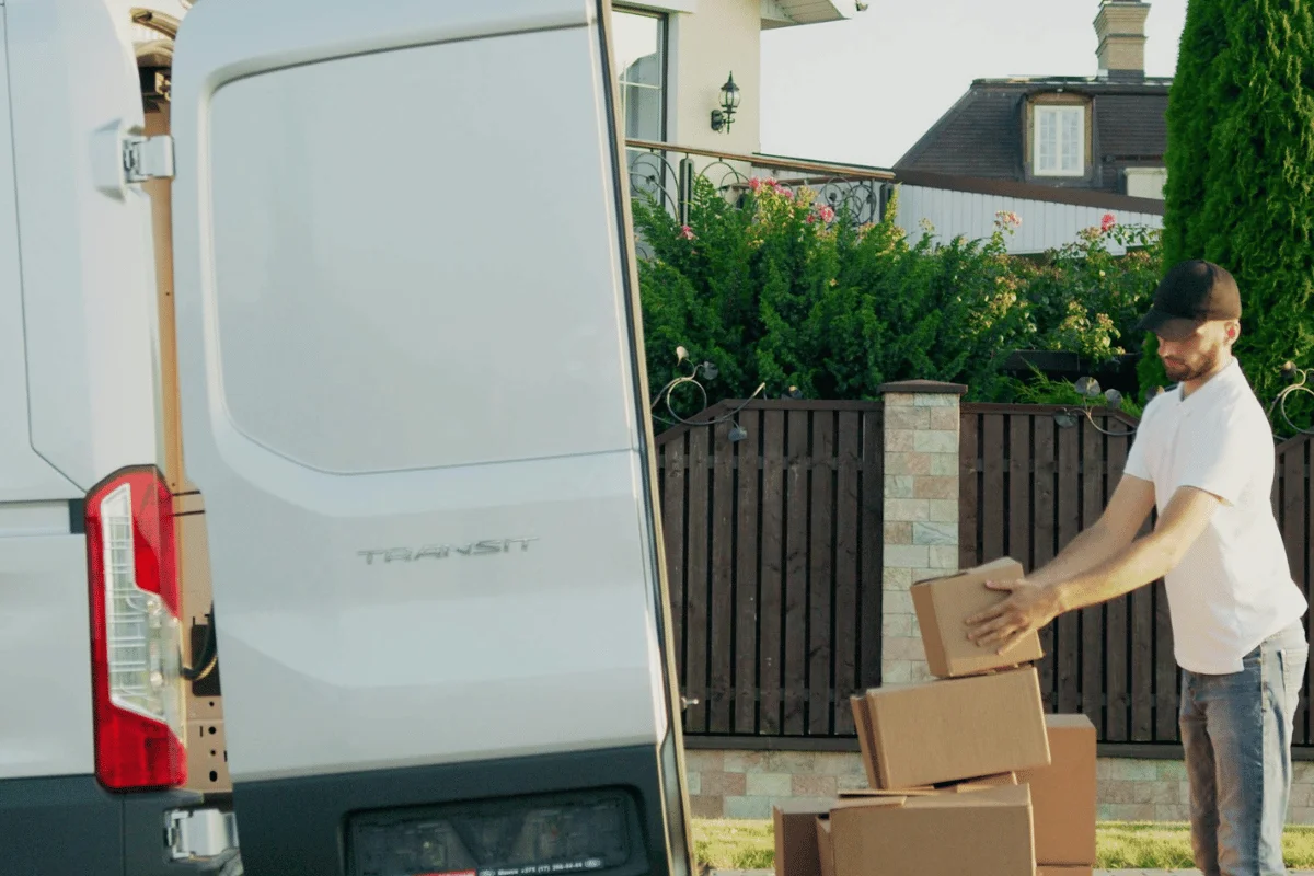 Delivery person stacking cardboard boxes outside a residential home.