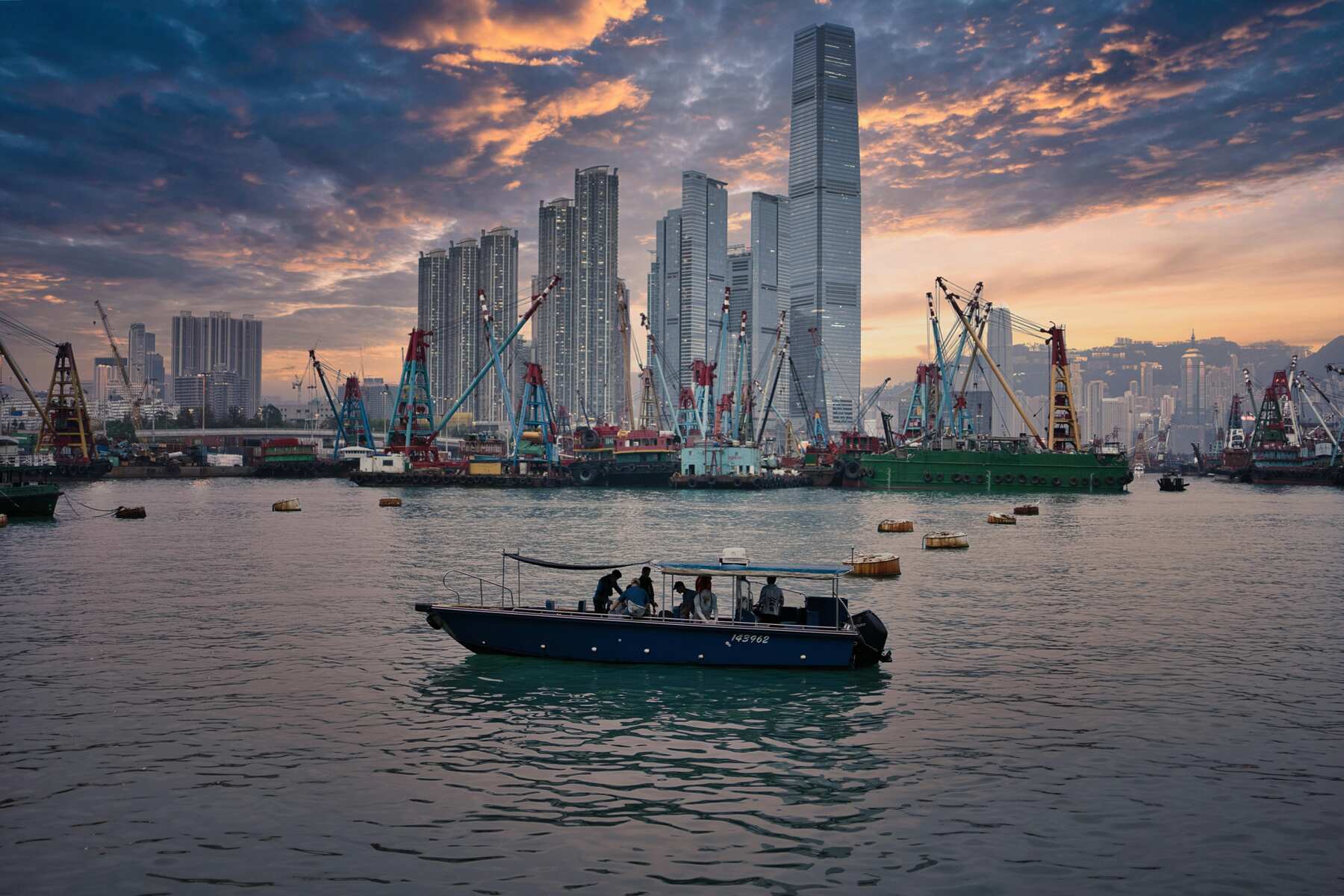 A cargo port in China at sunset, as seen from the sea, with a small boat sailing in front.