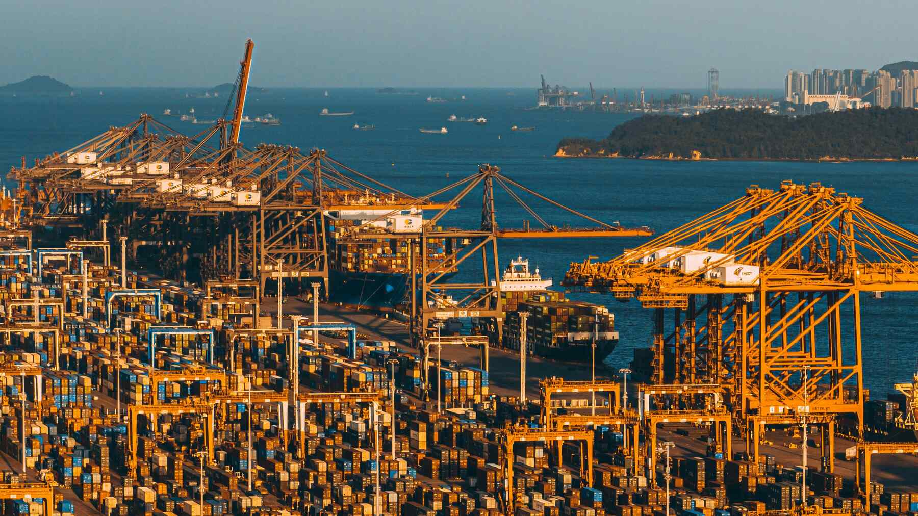 A port terminal jammed with containers, moored container ships fully loaded, and the sea beyond.