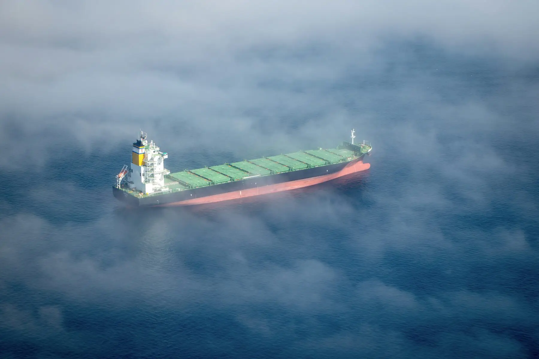 A cargo boat in the middle of the ocean seen from high up in the sky through clouds